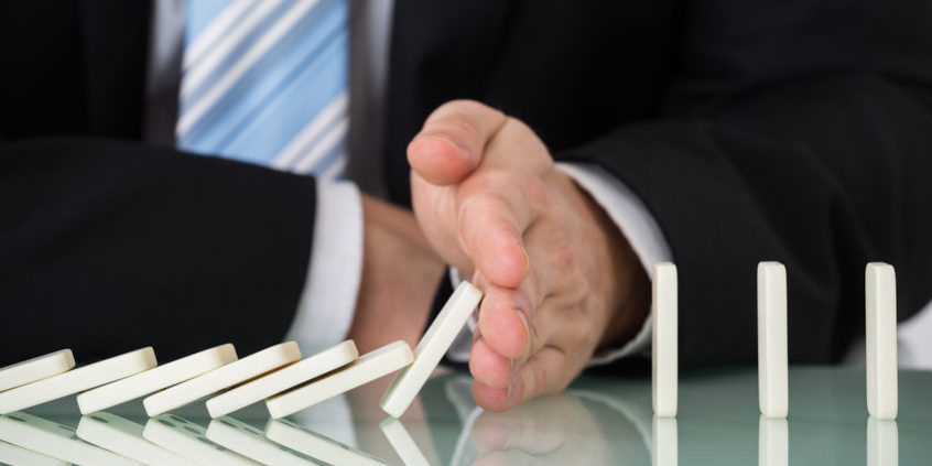 52273921 – close-up of businessperson stopping dominos falling on desk risk management