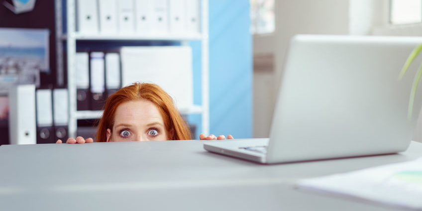 Young businesswoman peering over a desk in horror sell in may