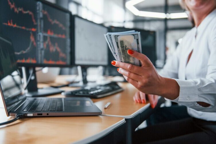 female trader holding cash in front of monitors | options trading mindset