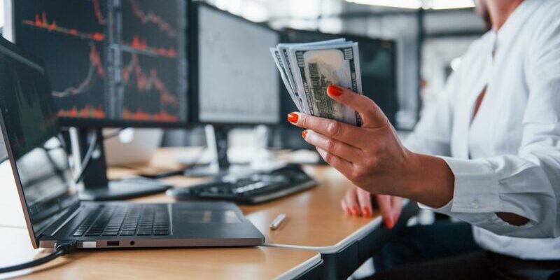 female trader holding cash in front of monitors | options trading mindset