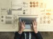 person typing on laptop surrounded by charts on desk | economic data points