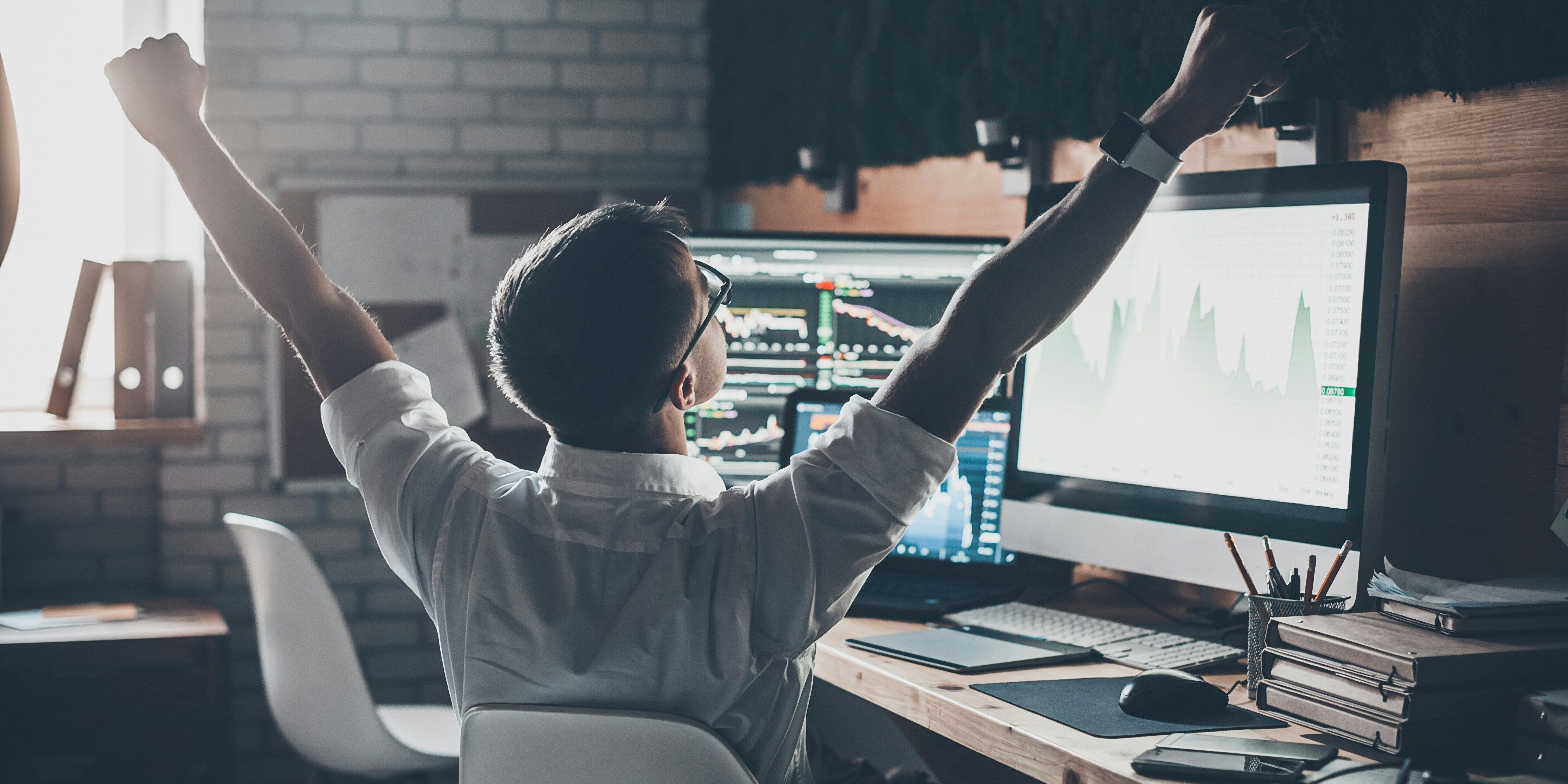 trader at desk raising arms in victory | bullish stock market signal