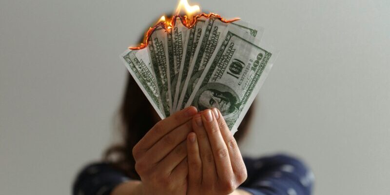 woman holding money that is burning | bad stock market news